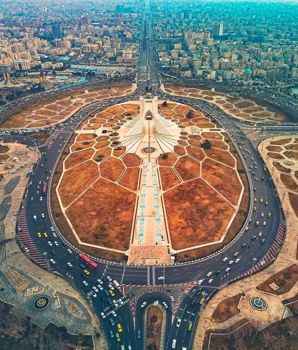 An aerial view shows a large circular plaza with geometric patterns surrounded by a multi-lane highway with cars — a public domain photograph from The Shah of Iran archive documenting the Pahlavi era.