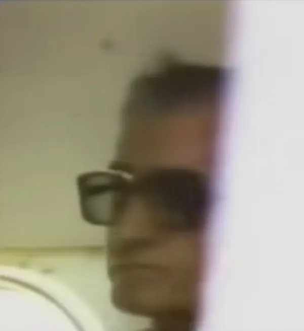 A blurry close-up of a person wearing dark-rimmed glasses, partially obscured by a white vertical edge — a public domain photograph from The Shah of Iran archive documenting the Pahlavi era.