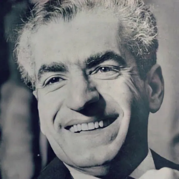 A close-up portrait of a smiling middle-aged man with grey hair wearing a dark suit jacket — a public domain photograph from The Shah of Iran archive documenting the Pahlavi era.