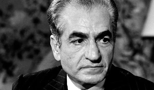 A close-up portrait of an older man with grey hair wearing a dark pinstripe jacket and white shirt — a public domain photograph from The Shah of Iran archive documenting the Pahlavi era.