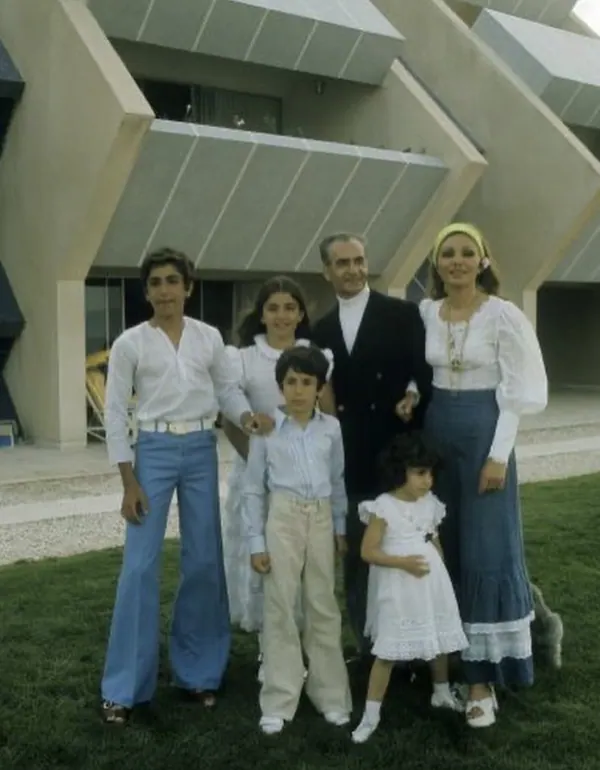 A family of six stands together on a lawn in front of a modern geometric building — a public domain photograph from The Shah of Iran archive documenting the Pahlavi era.