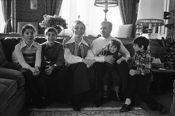 Five people of varying ages sit together on a sofa in a living room with lamps and curtains — a public domain photograph from The Shah of Iran archive documenting the Pahlavi era.