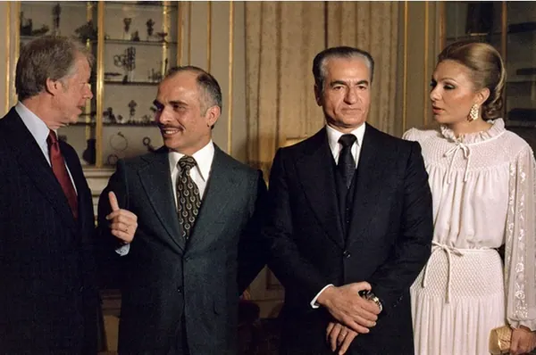 Four adults in formal attire stand together in a room with gold-trimmed walls and a display cabinet — a public domain photograph from The Shah of Iran archive documenting the Pahlavi era.