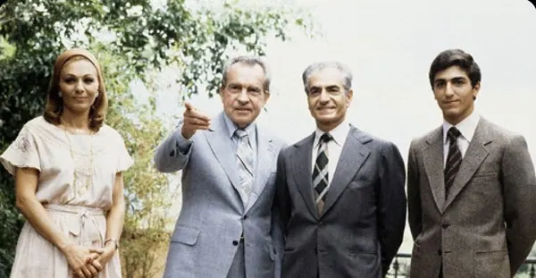 Four adults stand outdoors against a backdrop of green foliage, with one man pointing forward — a public domain photograph from The Shah of Iran archive documenting the Pahlavi era.