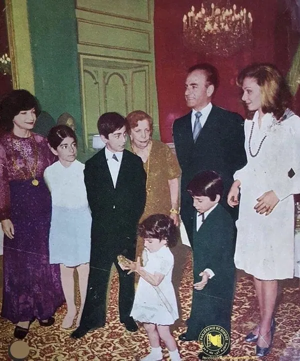 A group of adults and children in formal attire stand together in a room with a chandelier — a public domain photograph from The Shah of Iran archive documenting the Pahlavi era.