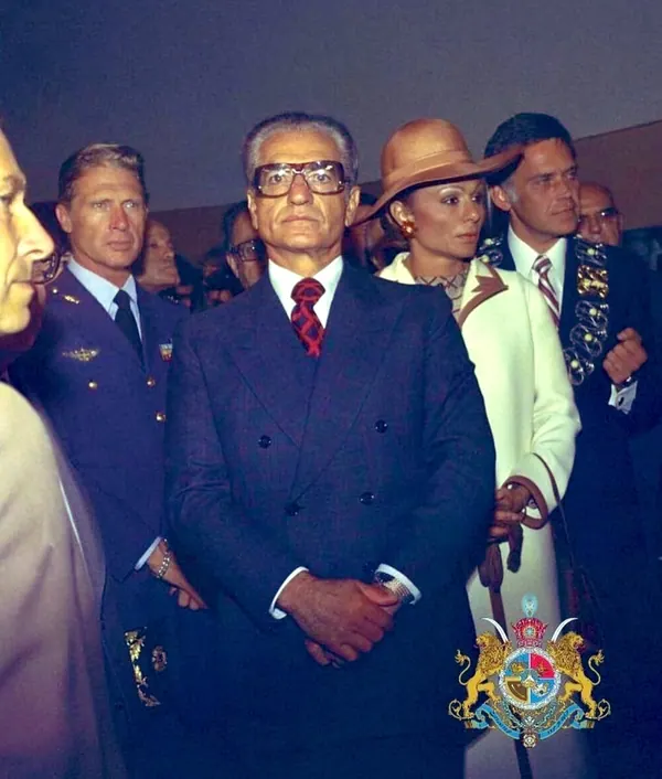 A group of adults in formal attire and uniforms stand together in a close composition — a public domain photograph from The Shah of Iran archive documenting the Pahlavi era.