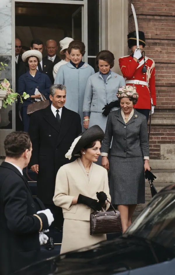 A group of formally dressed people exit a building while a uniformed guard stands at attention — a public domain photograph from The Shah of Iran archive documenting the Pahlavi era.