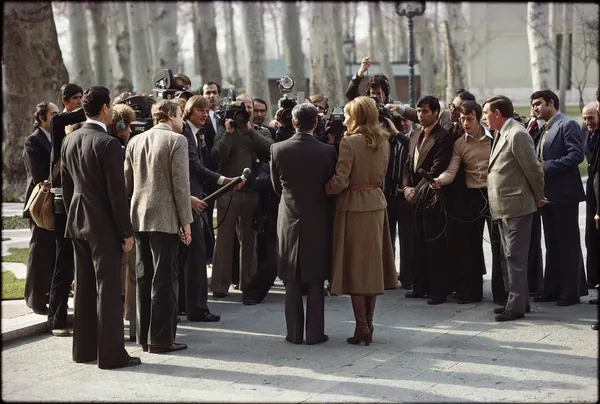 A group of people in formal attire stand outdoors with photographers and reporters holding cameras and microphones — a public domain photograph from The Shah of Iran archive documenting the Pahlavi era.