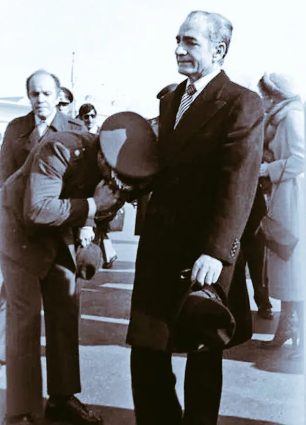 His Majesty, the Shah of Iran in a dark coat stands while another man in uniform bows deeply before him — a public domain photograph from The Shah of Iran archive documenting the Pahlavi era.
