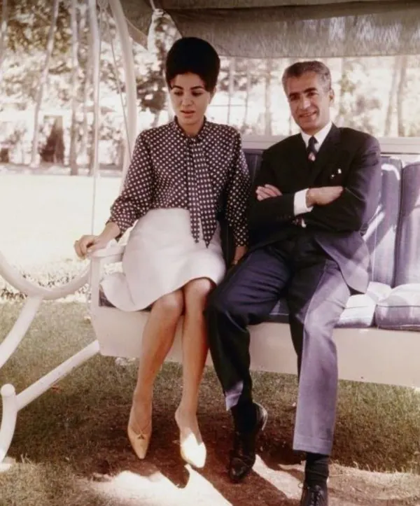 His Majesty, the Shah of Iran in a dark suit and Farah Pahlavi, Empress of Iran, in a polka-dot blouse sit on a garden swing — a public domain photograph from The Shah of Iran archive documenting the Pahlavi era.