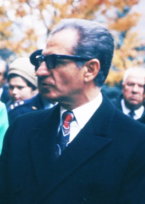 His Majesty, the Shah of Iran in a dark suit and sunglasses looks to the side with other people behind him — a public domain photograph from The Shah of Iran archive documenting the Pahlavi era.