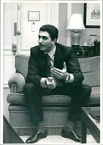 His Majesty, the Shah of Iran in a dark suit and tie sits on a striped sofa, gesturing with his hand — a public domain photograph from The Shah of Iran archive documenting the Pahlavi era.