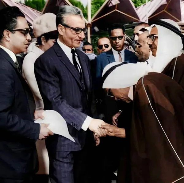 His Majesty, the Shah of Iran in a dark suit shakes hands with His Majesty wearing traditional brown robes and a white headcloth — a public domain photograph from The Shah of Iran archive documenting the Pahlavi era.