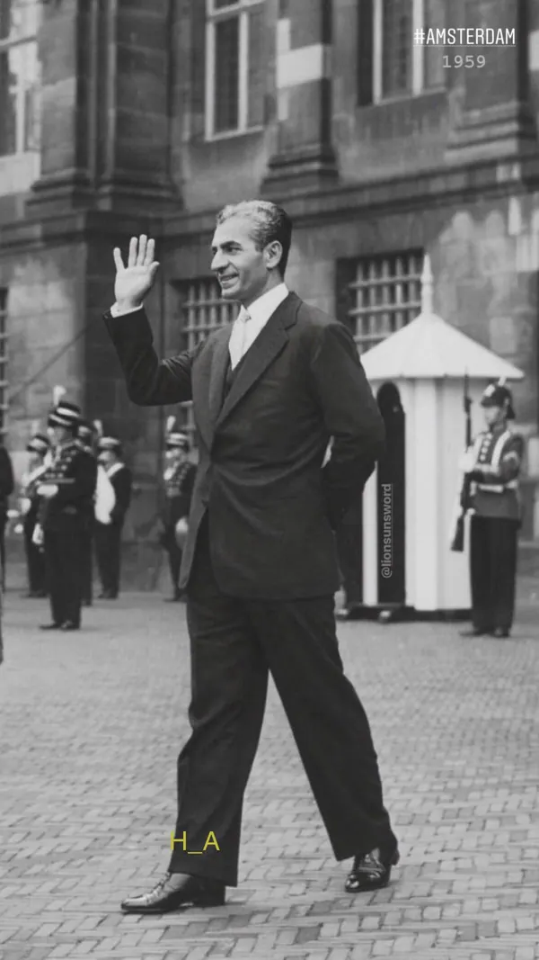 His Majesty, the Shah of Iran in a dark suit waves his hand while walking past uniformed guards in a courtyard — a public domain photograph from The Shah of Iran archive documenting the Pahlavi era.