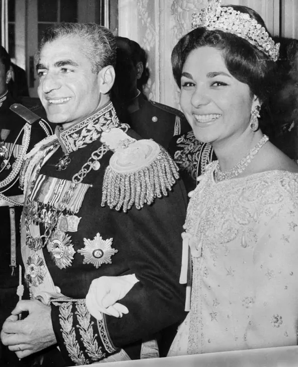 His Majesty, the Shah of Iran in a decorated military uniform and Farah Pahlavi, Empress of Iran, in a tiara and gown smile together — a public domain photograph from The Shah of Iran archive documenting the Pahlavi era.