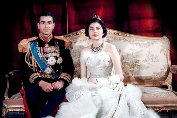 His Majesty, the Shah of Iran in a decorated military uniform and Farah Pahlavi, Empress of Iran, in a white gown sit on a sofa — a public domain photograph from The Shah of Iran archive documenting the Pahlavi era.
