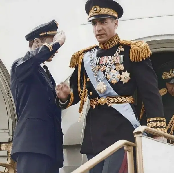 His Majesty, the Shah of Iran in a decorated military uniform exits a plane while another uniformed man salutes him — a public domain photograph from The Shah of Iran archive documenting the Pahlavi era.