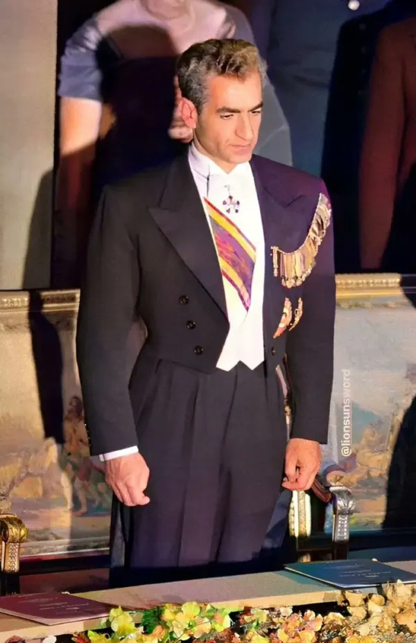 His Majesty, the Shah of Iran in a formal dark suit with a white waistcoat and medals stands before a painting — a public domain photograph from The Shah of Iran archive documenting the Pahlavi era.
