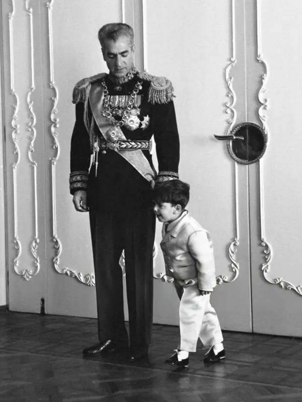 His Majesty, the Shah of Iran in a formal military uniform stands beside a young boy wearing a light-colored suit — a public domain photograph from The Shah of Iran archive documenting the Pahlavi era.