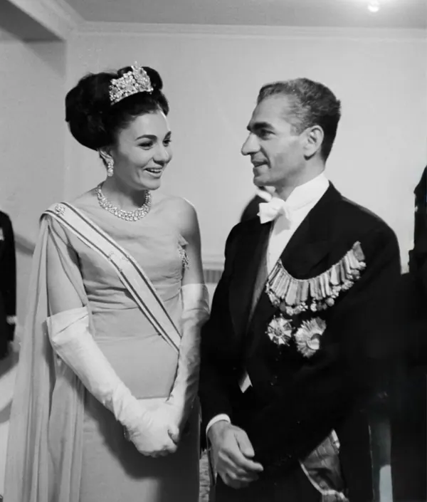 His Majesty, the Shah of Iran in a formal tuxedo and Farah Pahlavi, Empress of Iran, in a gown and tiara look at each other — a public domain photograph from The Shah of Iran archive documenting the Pahlavi era.