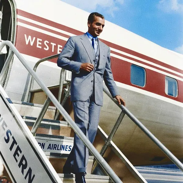 His Majesty, the Shah of Iran in a grey suit descends the stairs of a large white and red airplane — a public domain photograph from The Shah of Iran archive documenting the Pahlavi era.