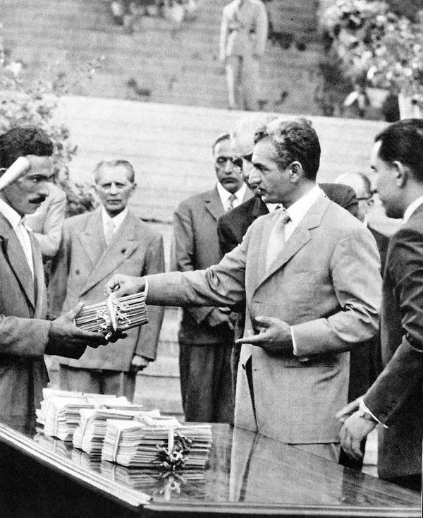 His Majesty, the Shah of Iran in a light suit hands a stack of keys to another man in a dark suit — a public domain photograph from The Shah of Iran archive documenting the Pahlavi era.