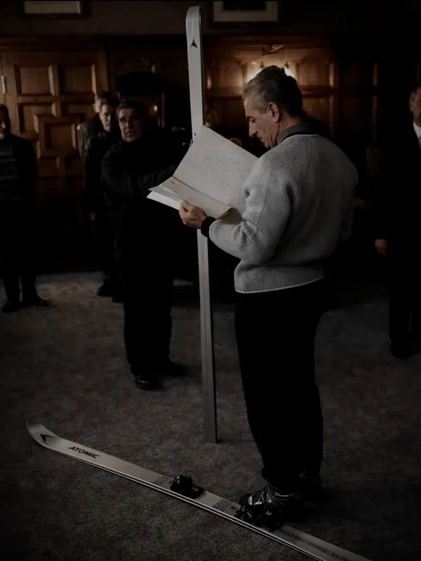 His Majesty, the Shah of Iran in a light sweater reads a document while standing on a ski in a dimly lit room — a public domain photograph from The Shah of Iran archive documenting the Pahlavi era.