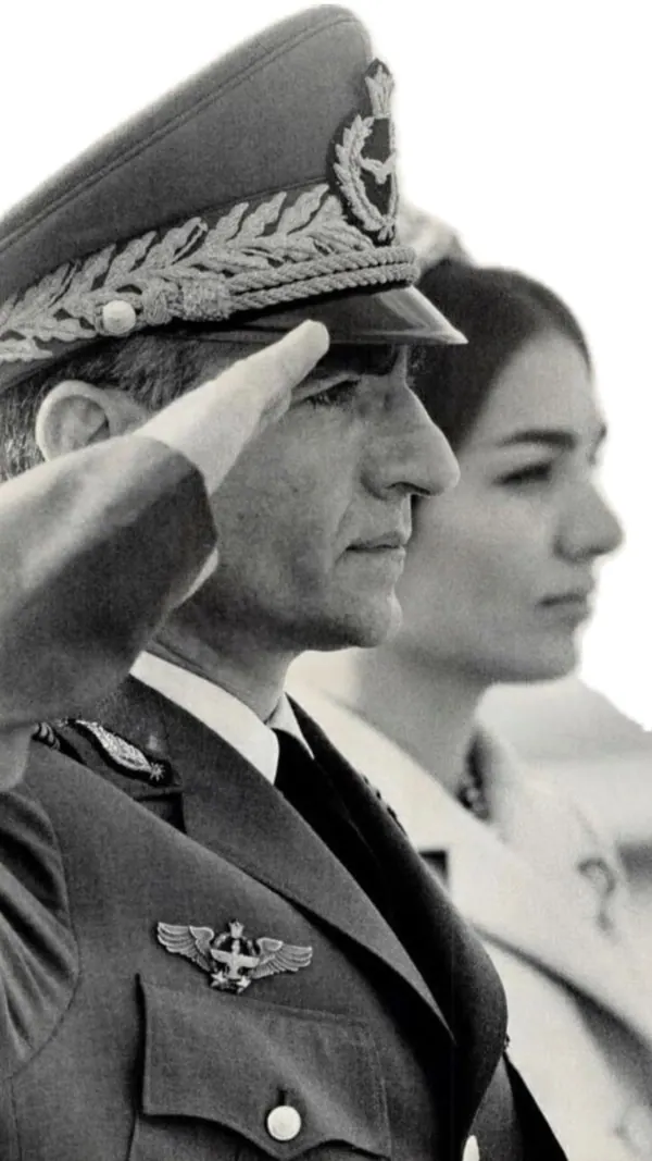 His Majesty, the Shah of Iran in a military uniform salutes while Farah Pahlavi, Empress of Iran, stands behind him in a profile view — a public domain photograph from The Shah of Iran archive documenting the Pahlavi era.