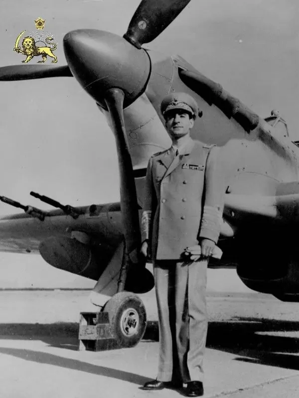 His Majesty, the Shah of Iran in a military uniform stands beside a propeller aircraft on a flat outdoor surface — a public domain photograph from The Shah of Iran archive documenting the Pahlavi era.