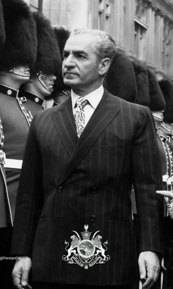 His Majesty, the Shah of Iran in a pinstripe suit and patterned tie stands before a line of uniformed guards in tall hats — a public domain photograph from The Shah of Iran archive documenting the Pahlavi era.