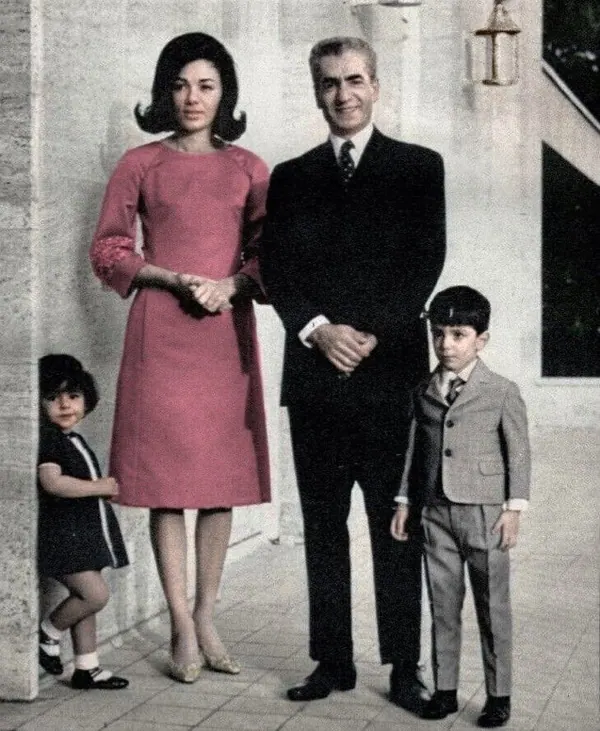 His Majesty, the Shah of Iran in a suit, Farah Pahlavi, Empress of Iran, in a pink dress, and two children stand together outdoors — a public domain photograph from The Shah of Iran archive documenting the Pahlavi era.