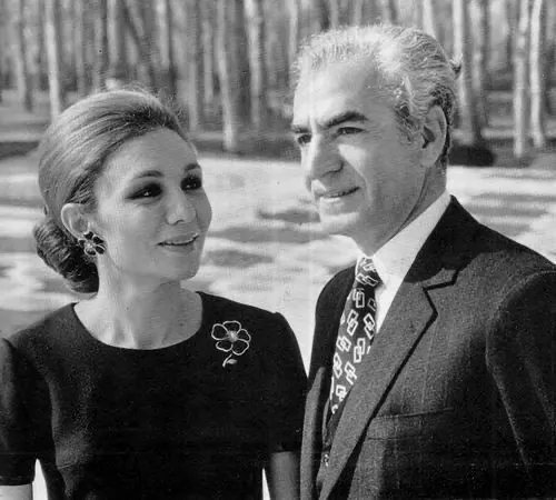 His Majesty, the Shah of Iran in a suit and Farah Pahlavi, Empress of Iran, in a dark dress stand together outdoors near trees — a public domain photograph from The Shah of Iran archive documenting the Pahlavi era.
