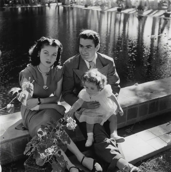 His Majesty, the Shah of Iran in a suit and Farah Pahlavi, Empress of Iran, in a dress sit by a pond with a small child — a public domain photograph from The Shah of Iran archive documenting the Pahlavi era.