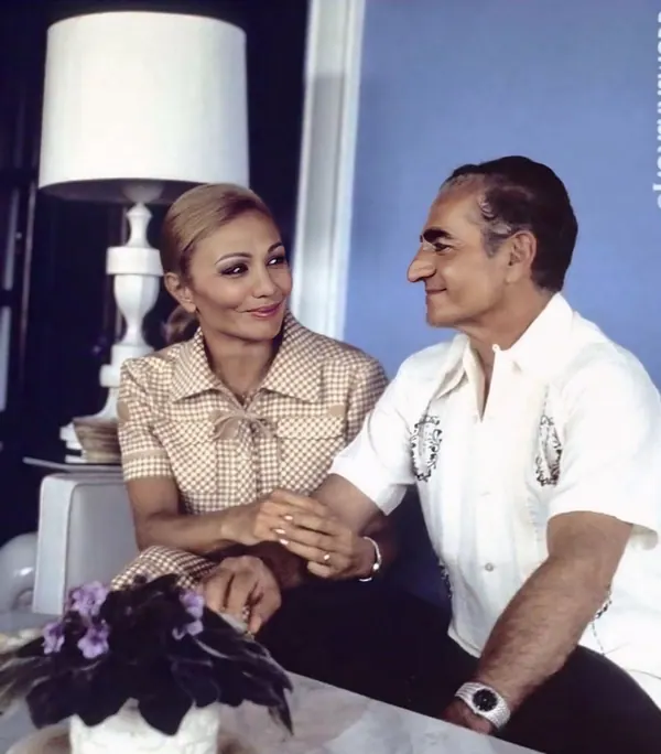 His Majesty, the Shah of Iran in a white shirt and Farah Pahlavi, Empress of Iran, in a checkered dress hold hands while looking at each other — a public domain photograph from The Shah of Iran archive documenting the Pahlavi era.