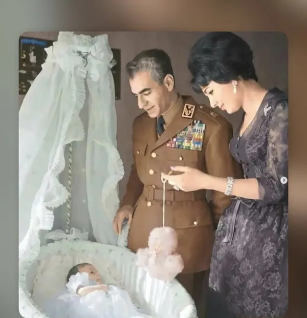 His Majesty, the Shah of Iran in military uniform and Farah Pahlavi, Empress of Iran, in a lace dress look at a baby in a bassinet — a public domain photograph from The Shah of Iran archive documenting the Pahlavi era.