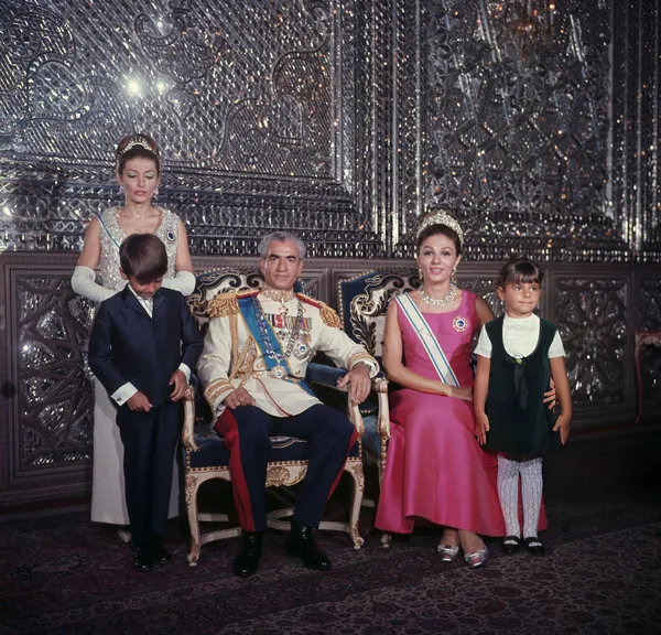 His Majesty, the Shah of Iran in military uniform sits between two women in gowns and two children against a mirrored wall — a public domain photograph from The Shah of Iran archive documenting the Pahlavi era.