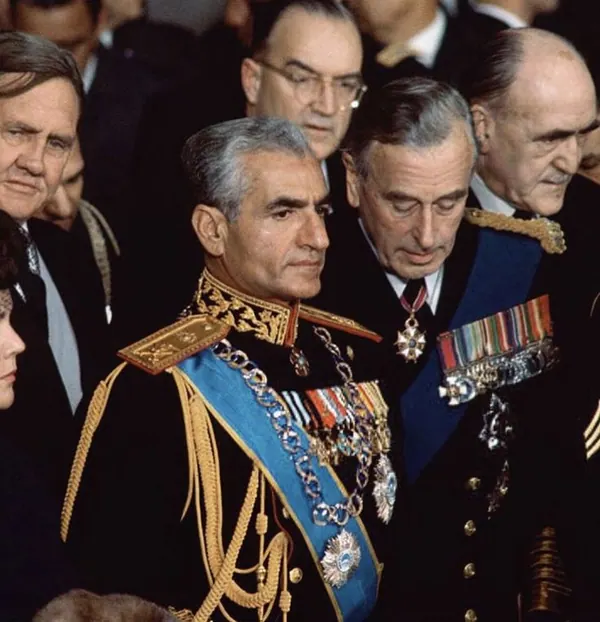 Men in formal military uniforms and suits stand close together in a crowded indoor setting — a public domain photograph from The Shah of Iran archive documenting the Pahlavi era.