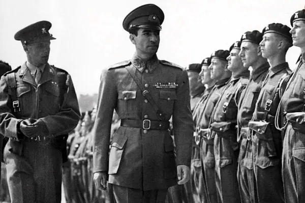 Men in military uniforms stand in formation, with one man standing prominently in the center foreground — a public domain photograph from The Shah of Iran archive documenting the Pahlavi era.