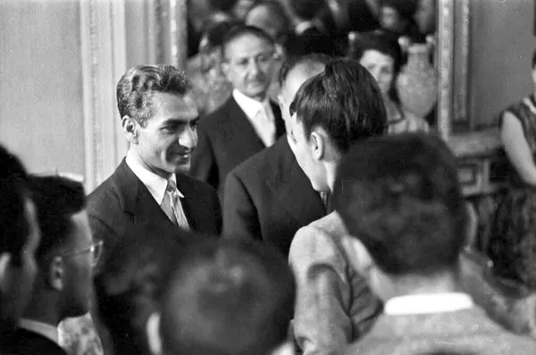 Men in suits and formal attire stand close together in a room with a mirror in the background — a public domain photograph from The Shah of Iran archive documenting the Pahlavi era.