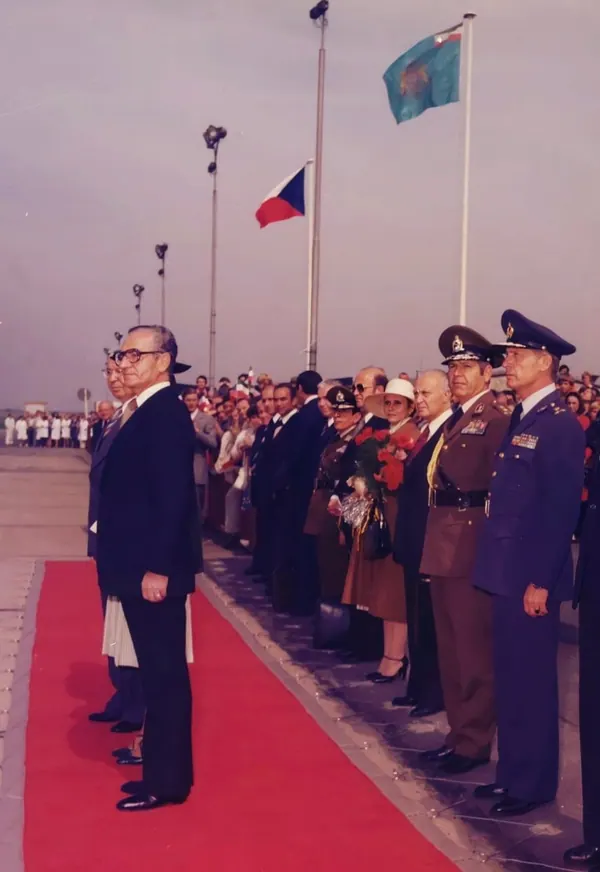 Men in suits and military uniforms stand in a line beside a red carpet under two flags — a public domain photograph from The Shah of Iran archive documenting the Pahlavi era.