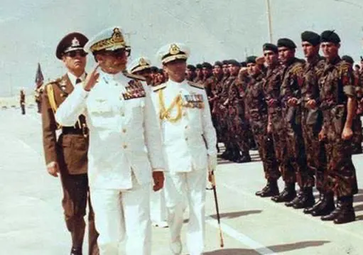 Men in white dress uniforms walk past a line of soldiers in camouflage gear on a paved area — a public domain photograph from The Shah of Iran archive documenting the Pahlavi era.