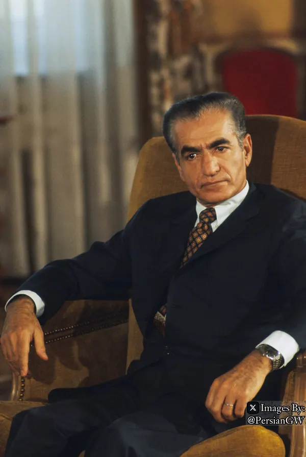 His Majesty, the Shah of Iran in a dark suit and patterned tie sits leaning back in a tan armchair — a public domain photograph from The Shah of Iran archive documenting the Pahlavi era.