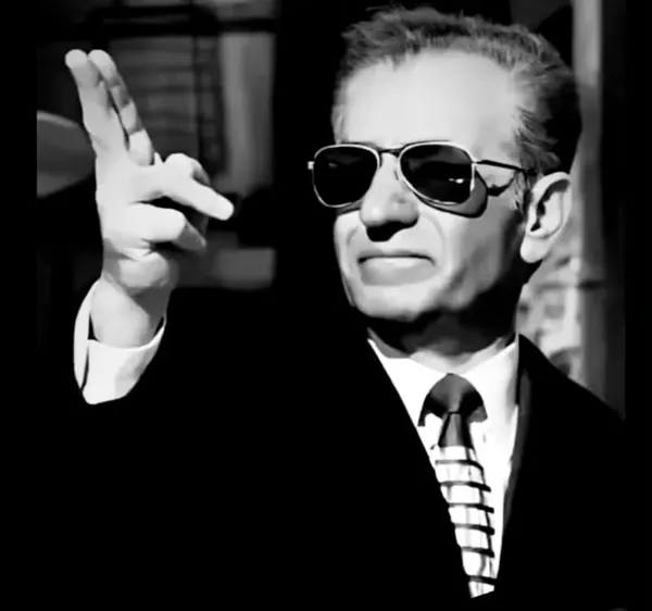 His Majesty, the Shah of Iran in a dark suit and sunglasses raises his hand with fingers extended — a public domain photograph from The Shah of Iran archive documenting the Pahlavi era.