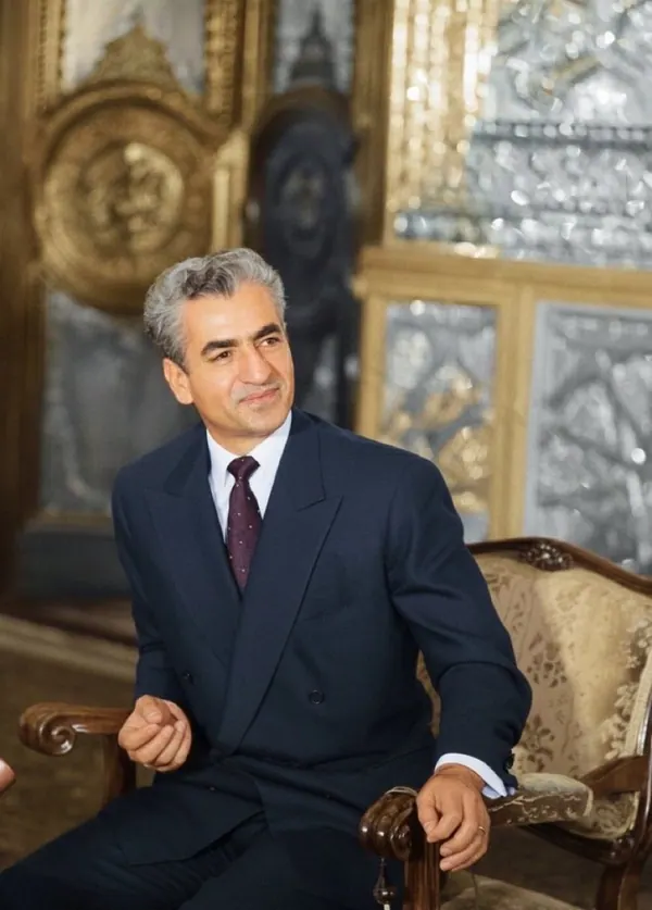 His Majesty, the Shah of Iran in a dark suit and tie sits in an ornate chair within a lavish room — a public domain photograph from The Shah of Iran archive documenting the Pahlavi era.