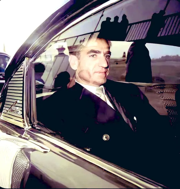 His Majesty, the Shah of Iran in a dark suit and tie sits inside a vintage car — a public domain photograph from The Shah of Iran archive documenting the Pahlavi era.