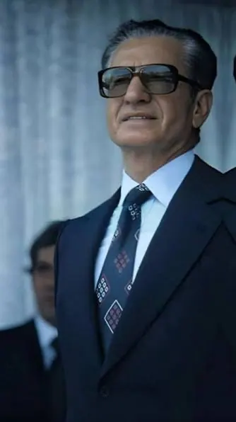His Majesty, the Shah of Iran in a dark suit, white shirt, and patterned tie wears dark sunglasses — a public domain photograph from The Shah of Iran archive documenting the Pahlavi era.