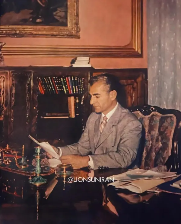 His Majesty, the Shah of Iran in a grey suit sits at a desk reading a document in a study — a public domain photograph from The Shah of Iran archive documenting the Pahlavi era.