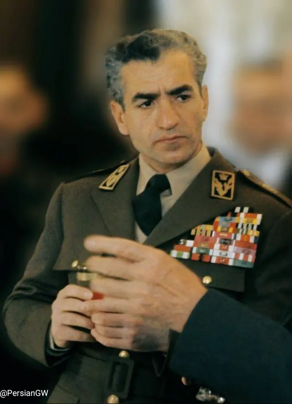 His Majesty, the Shah of Iran in a military uniform with medals on his chest holds a small object — a public domain photograph from The Shah of Iran archive documenting the Pahlavi era.