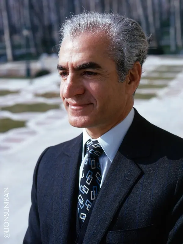His Majesty, the Shah of Iran in a pinstripe suit and patterned tie looks away from the camera outdoors — a public domain photograph from The Shah of Iran archive documenting the Pahlavi era.