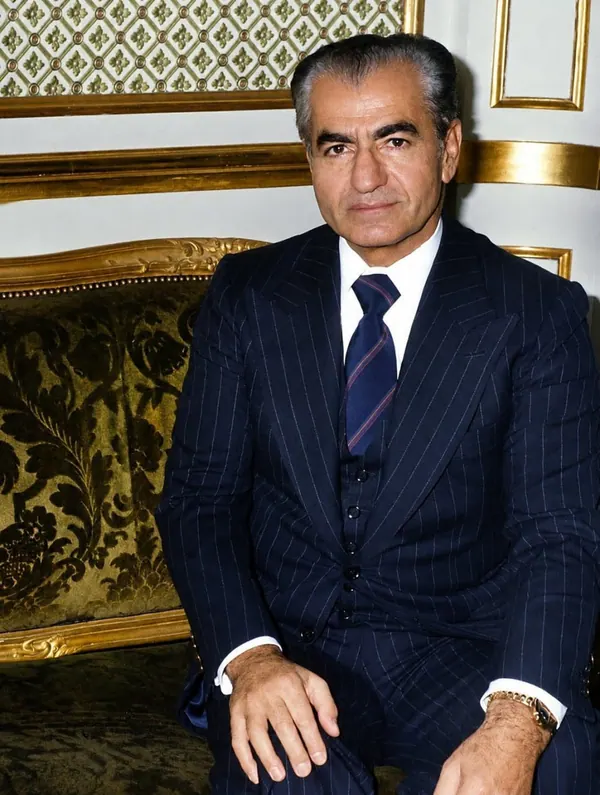 His Majesty, the Shah of Iran in a pinstripe suit and tie sits on an ornate gold-trimmed sofa — a public domain photograph from The Shah of Iran archive documenting the Pahlavi era.